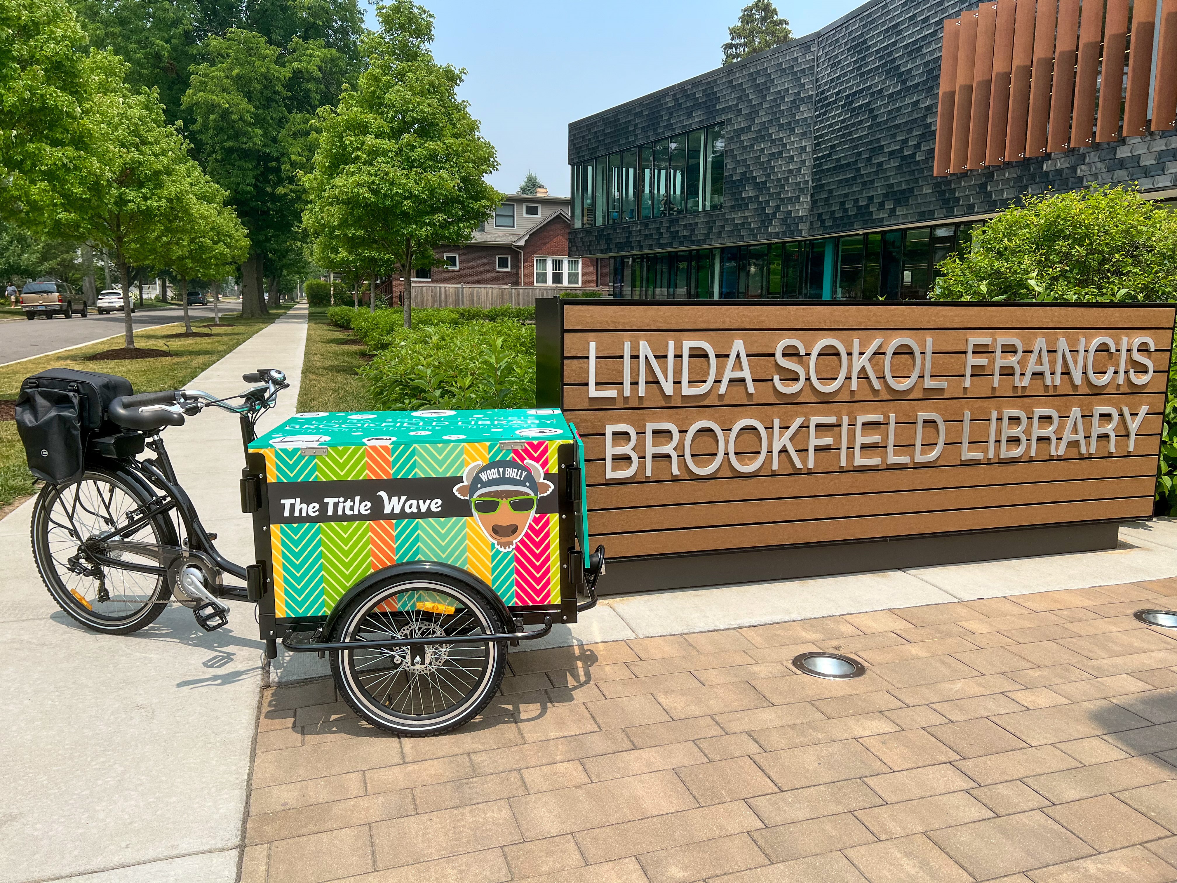 Immagine della bici della biblioteca accanto al cartello con la scritta Linda Sokol Francis Brookfield Library con l'edificio della biblioteca sullo sfondo
